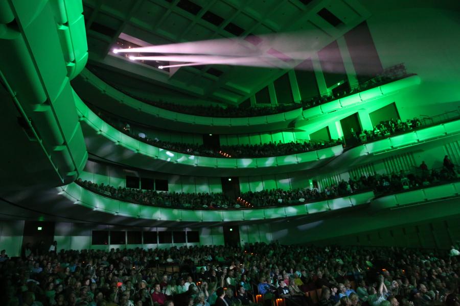 A view of the audience during a rock concert. An emerald green light glows against the balconies full of people.