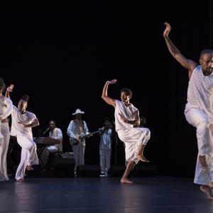 A group of five dancers wearing all white perform on stage.