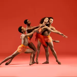 Four Dance Theatre of Harlem dancers perform together in front of an orange background.
