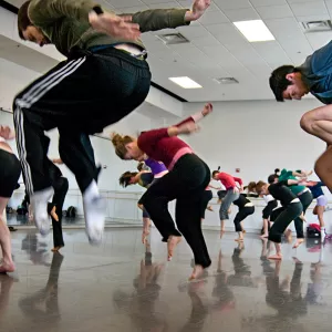 Dance students looking down and jumping with arms stretched behind them
